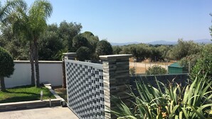 A gated outdoor area with a view of distant mountains, a concrete pathway, and a variety of trees.