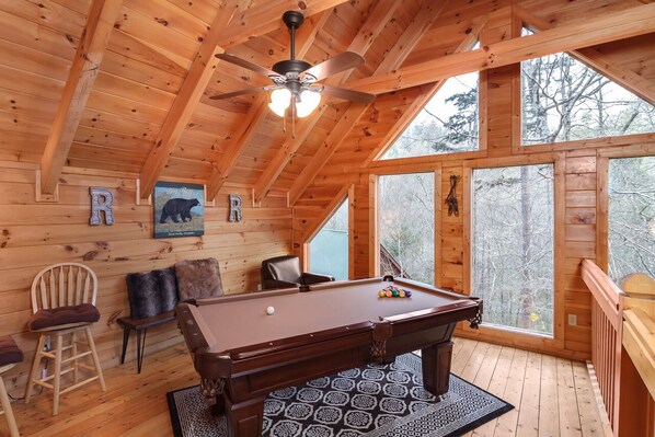 A wooden interior with a pool table, chairs, and a ceiling fan.