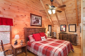 A cozy wooden cabin bedroom with a bed, a ceiling fan, and a framed picture on the wall.