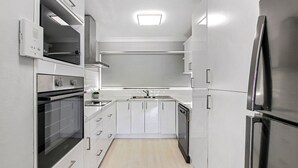 Une cuisine moderne avec des meubles blancs, des appareils en acier inoxydable et un plancher en bois clair.