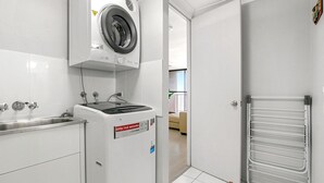 Un espace buanderie comprenant un lave-linge à chargement frontal, un évier et un étendoir.