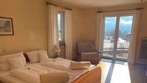 A hotel room with a wooden bed, a chair, and a view of the outside through a sliding glass door. - Holiday house with 2 bedrooms, terrace and balcony, 150 m² (Inzell)