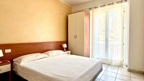 Een slaapkamer met een bed, nachtkastje, kledingkast en een raam met uitzicht.