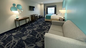 Una habitación de hotel con cama, escritorio, silla, sofá y televisión en la pared.