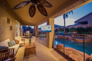 An outdoor patio area with a pool, seating, and a television screen.