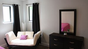 Une chambre à coucher comprenant un lit, une commode, un miroir et deux fenêtres avec des rideaux.