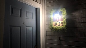 Une porte en bois sombre, ornée d’un cadre blanc et d’une plaque numérotée « 1825 » fixée au mur.