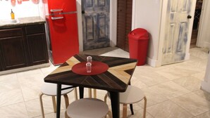 Un coin repas comprenant une table carrée, quatre chaises, un réfrigérateur rouge et une poubelle rouge.