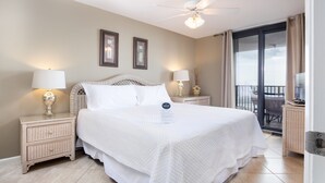 Habitación de hotel con una cama grande, dos mesitas de noche con lámparas, un ventilador de techo y vistas al exterior a través de una puerta corrediza de vidrio.