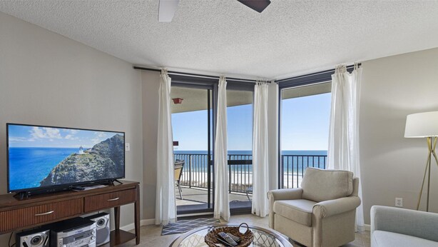 Habitación de hotel con televisión, una silla, una lámpara y balcón con vista al océano.