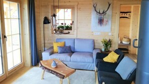A cozy room with a sofa, a coffee table, and a chair. There's a window with curtains, a painting of a deer on the wall, and a plant on the floor.