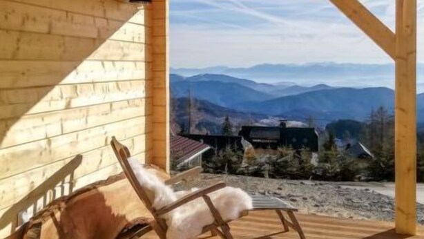 A wooden cabin with a wooden deck and a rocking chair.