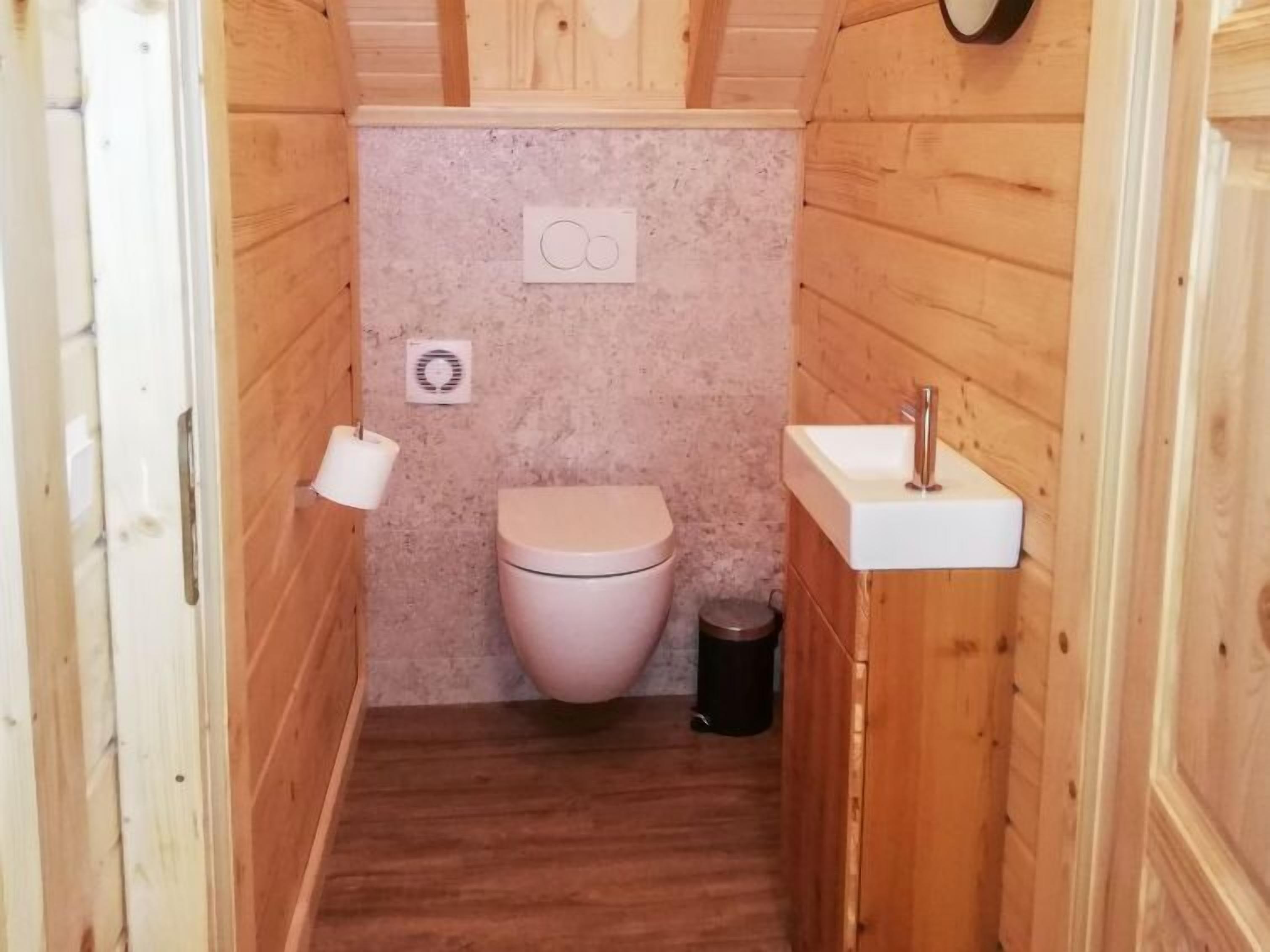 Pieni kylpyhuone, jonka seinät on paneloitu puulla. Siellä on wc, pesuallas ja roskakori.