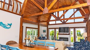 Un'ampia stanza con soffitto in legno, un tavolo da pranzo con sedie blu, un divano con decorazioni a stella marina e un camino.