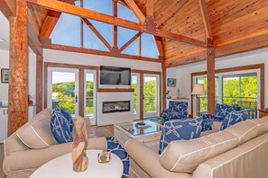 A spacious living room with a high ceiling, large windows, a fireplace, and comfortable seating. - Custom built home with expansive views of South Bald Head. Open concept, plenty of space for family (Bald Head Island)