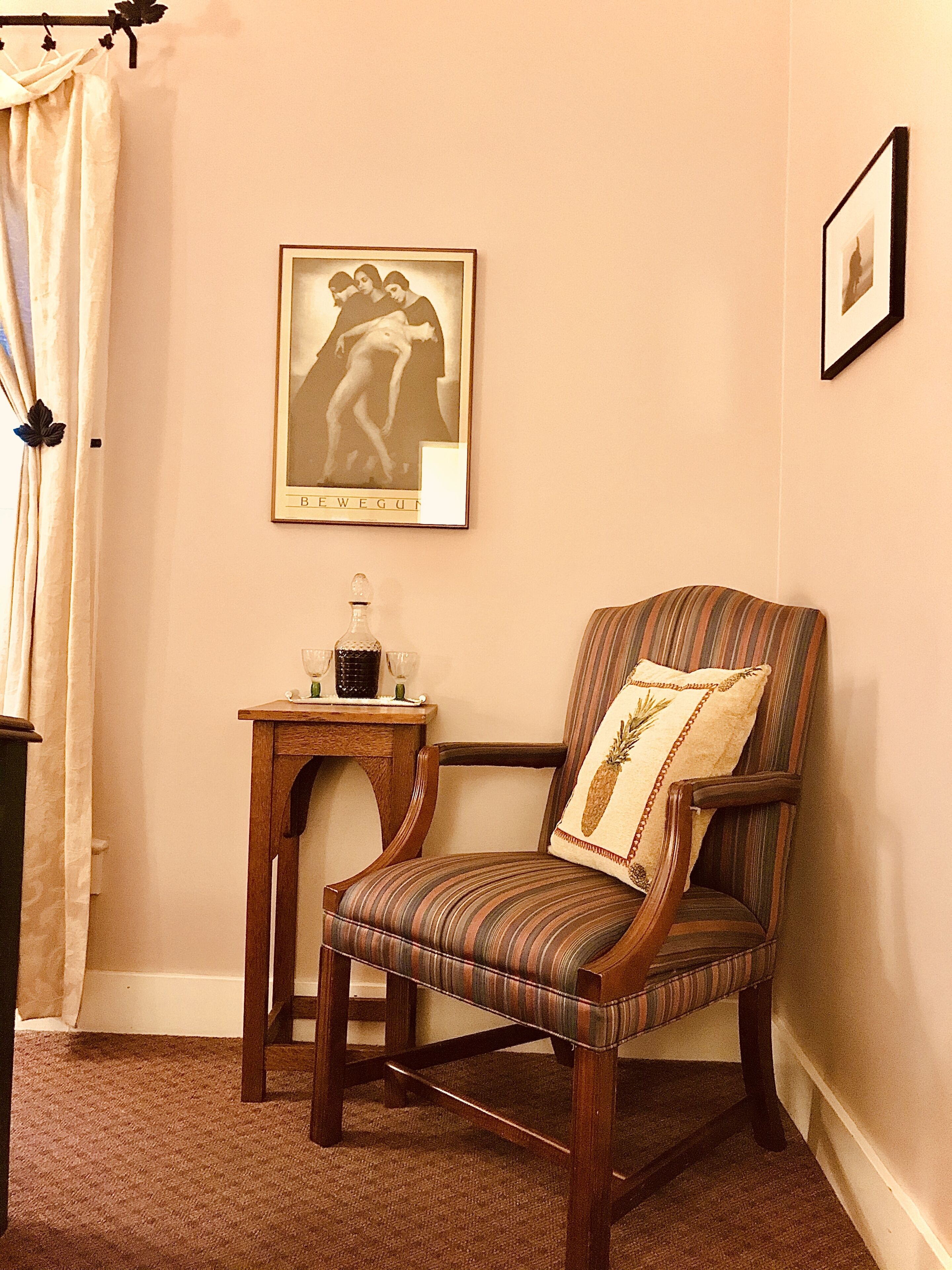 Une pièce d’angle avec une chaise en bois, une petite table sur laquelle se trouve un verre, et un tableau encadré accroché au mur.