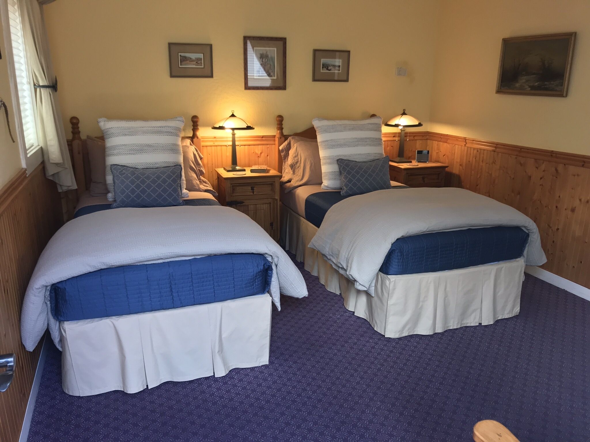 A double room with two beds, a wooden headboard, a nightstand with a lamp, and a framed picture on the wall.