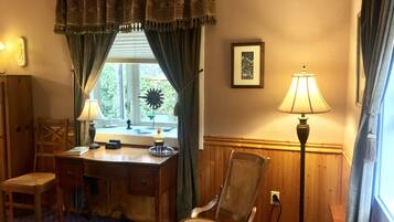 A room with a wooden desk, a wicker chair, a lamp, and a window with curtains.