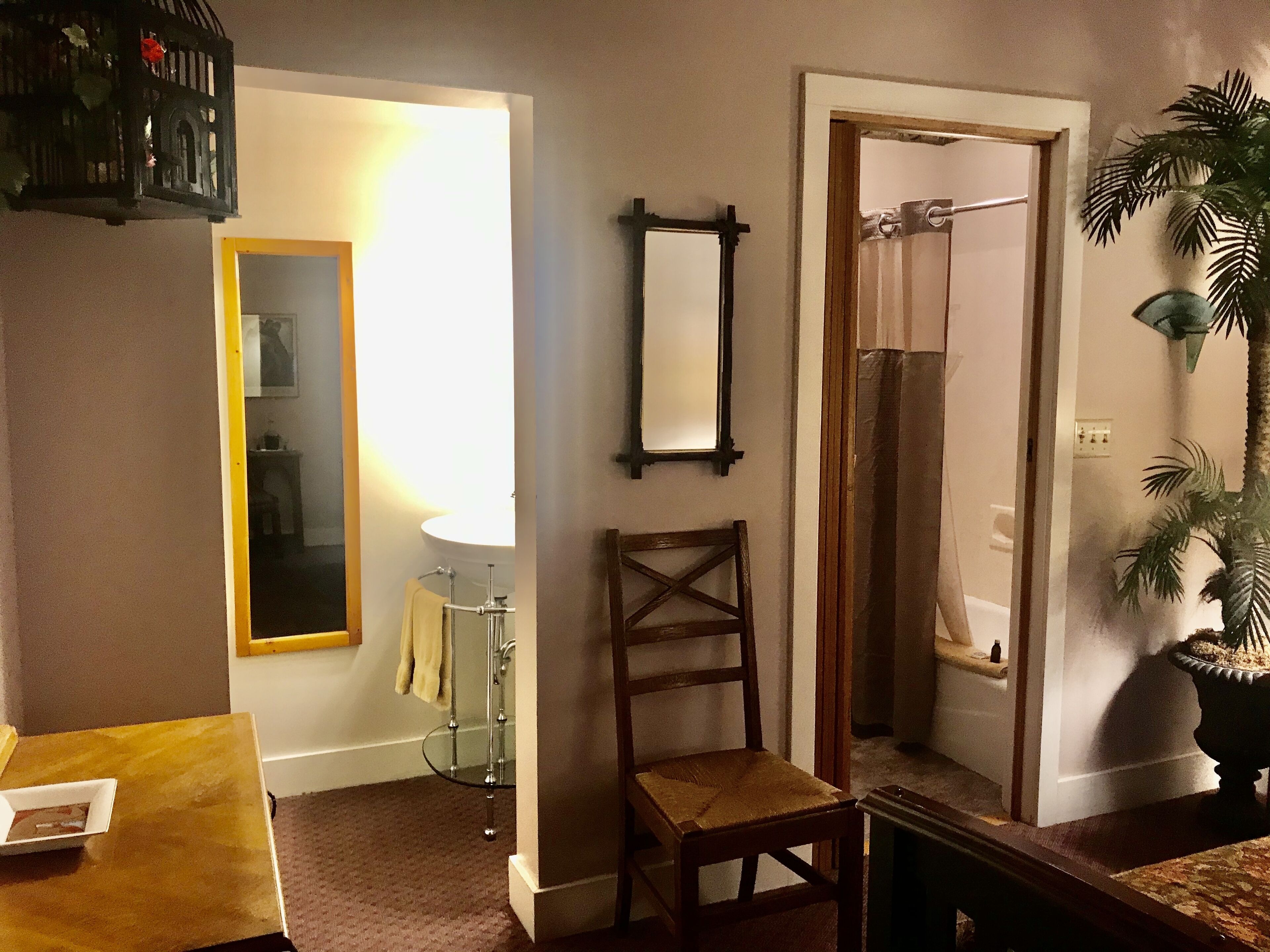 A room with a wooden chair, a mirror, a glass table, and a potted plant.