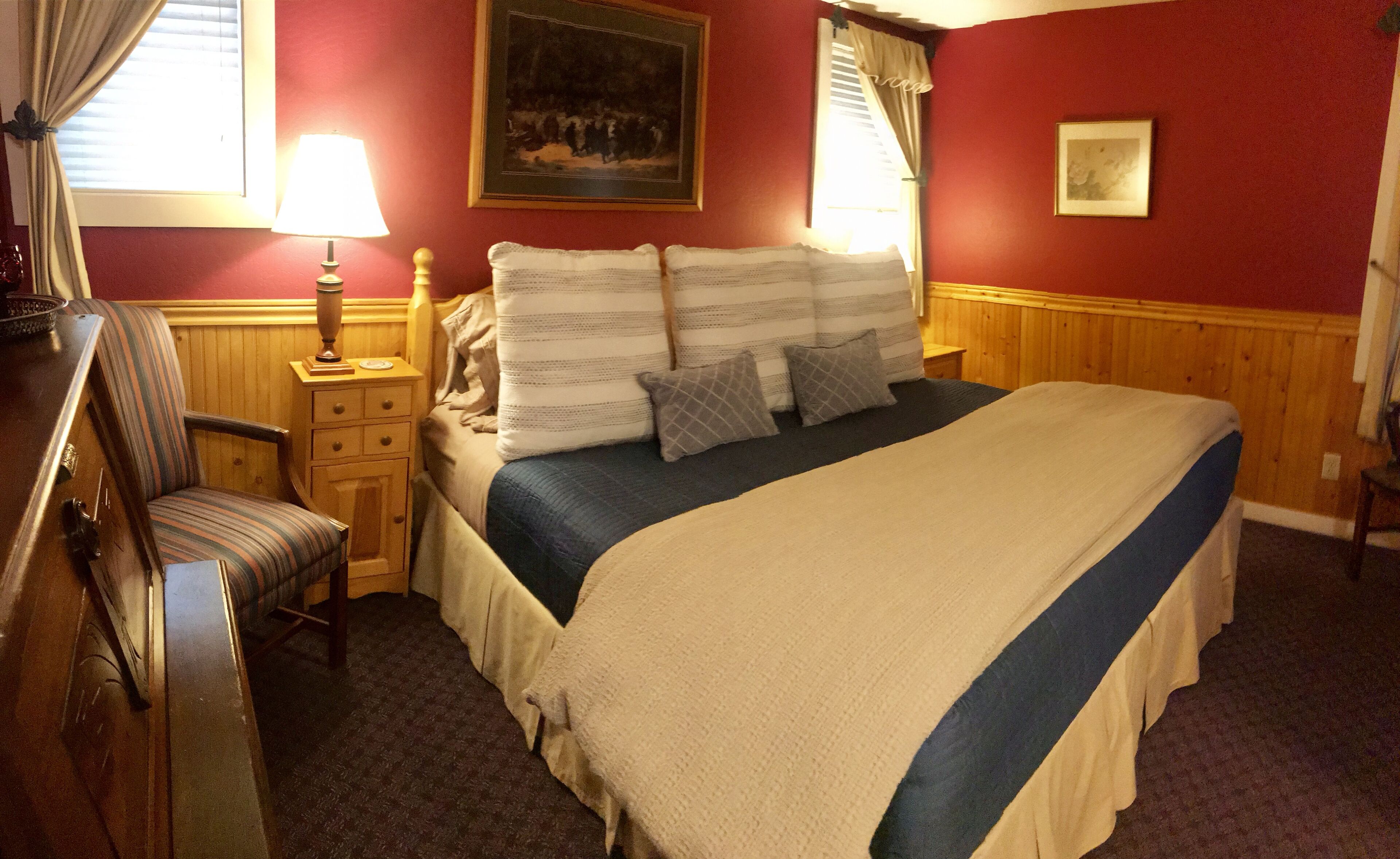 A hotel room with a large bed, a nightstand, a chair, and a lamp.