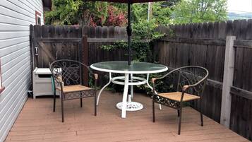 A patio with a round table and two chairs, an umbrella, and a wooden fence.