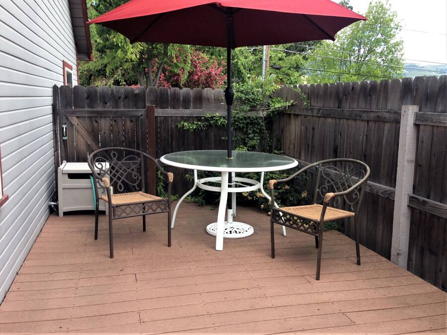 A patio with a round table and two chairs, an umbrella, and a wooden fence.