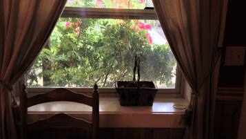 A window with curtains, a wooden chair, and a small table with a basket.