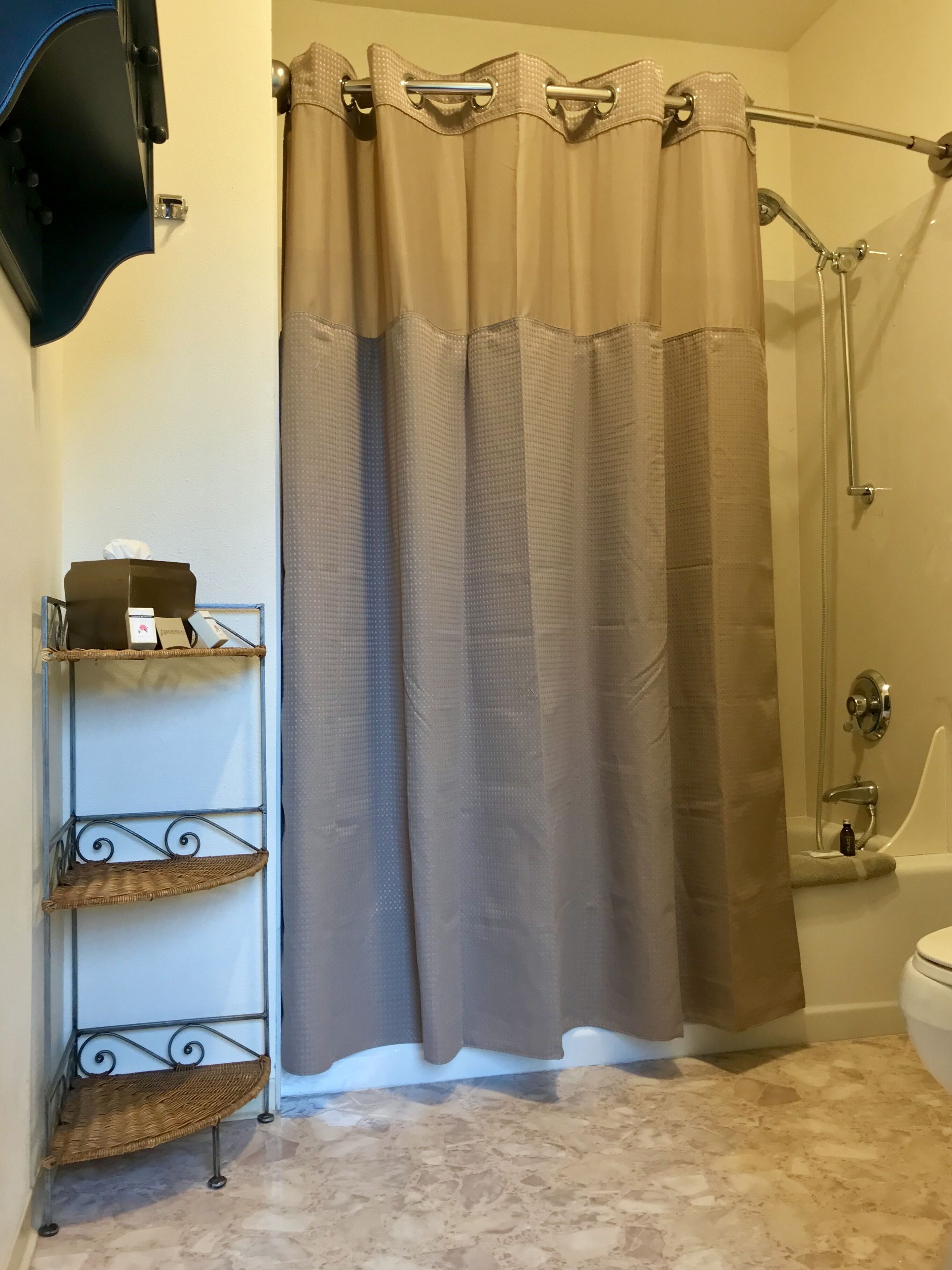 A bathroom with a beige shower curtain, a metal shelf unit, and a bathtub.