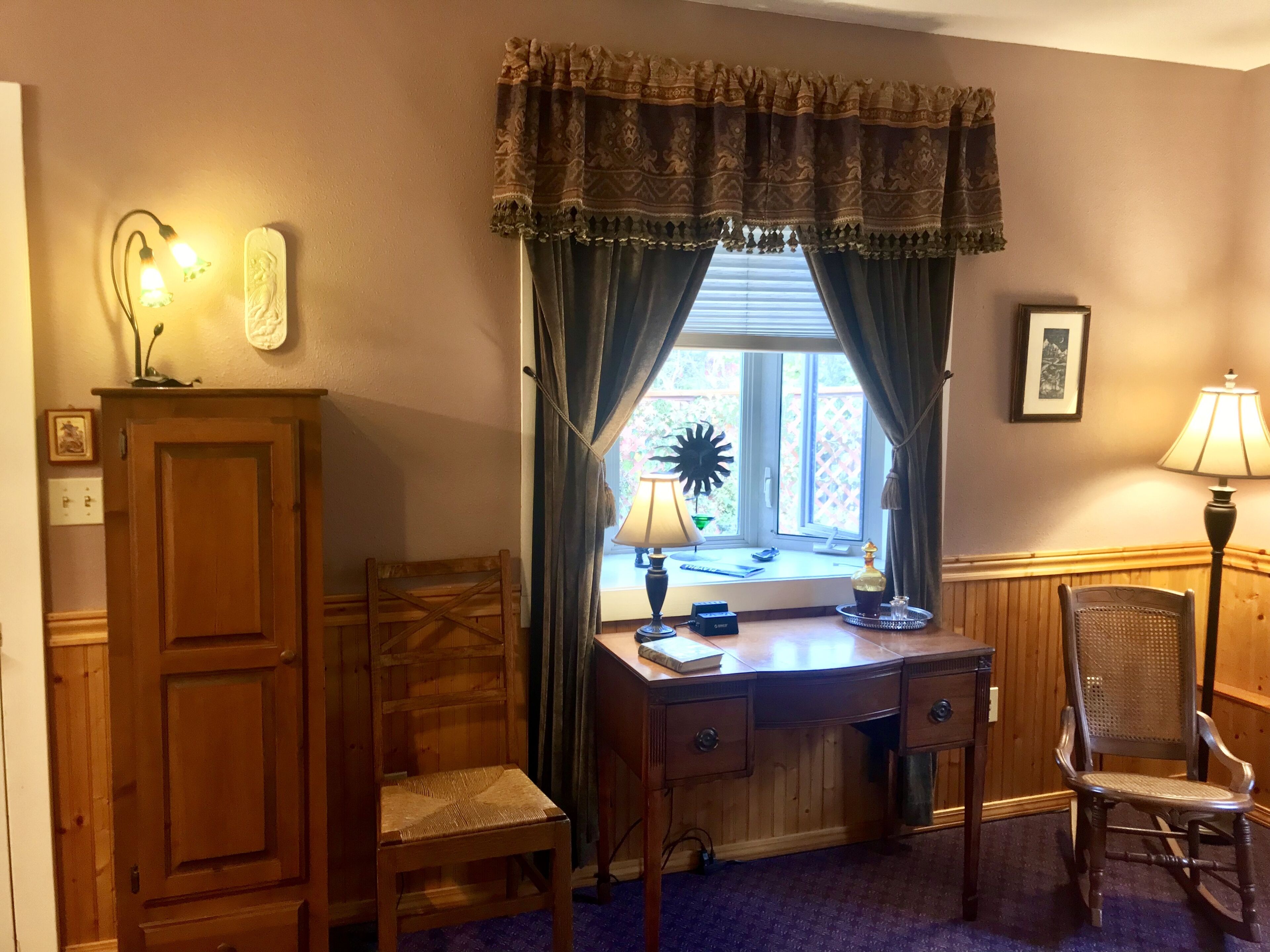 A room with a wooden desk, two chairs, a lamp, and a window with curtains.