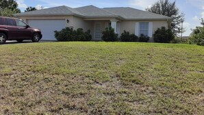 A residential house with a garage, a lawn, and a parked car. - Alabama Rd S Rancher (Lehigh Acres)