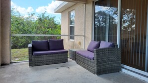 A balcony with wicker furniture and a view of greenery. - Alabama Rd S Rancher (Lehigh Acres)
