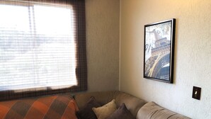 Habitación de esquina con sofá, un cuadro enmarcado en la pared y una ventana con persianas.