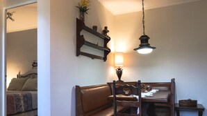 Un comedor con una mesa y sillas de madera, una lámpara colgante y un estante en la pared con adornos.