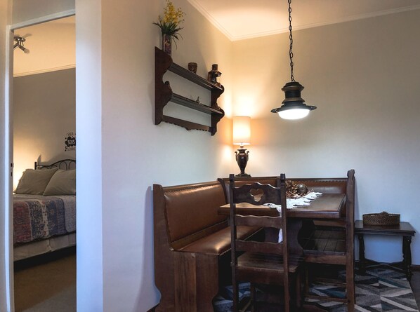 Un coin repas avec une table et des chaises en bois, un luminaire suspendu et une étagère murale agrémentée d’objets décoratifs.