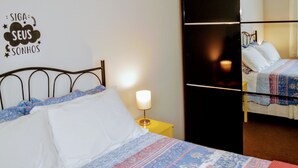 Habitación de hotel con una cama, una mesita de noche con una lámpara, un refrigerador negro y una pared con un letrero decorativo.