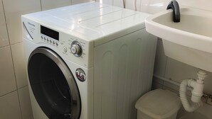 Un área de lavandería compacta con lavadora de carga frontal, un lavamanos pequeño y un cubo de basura.