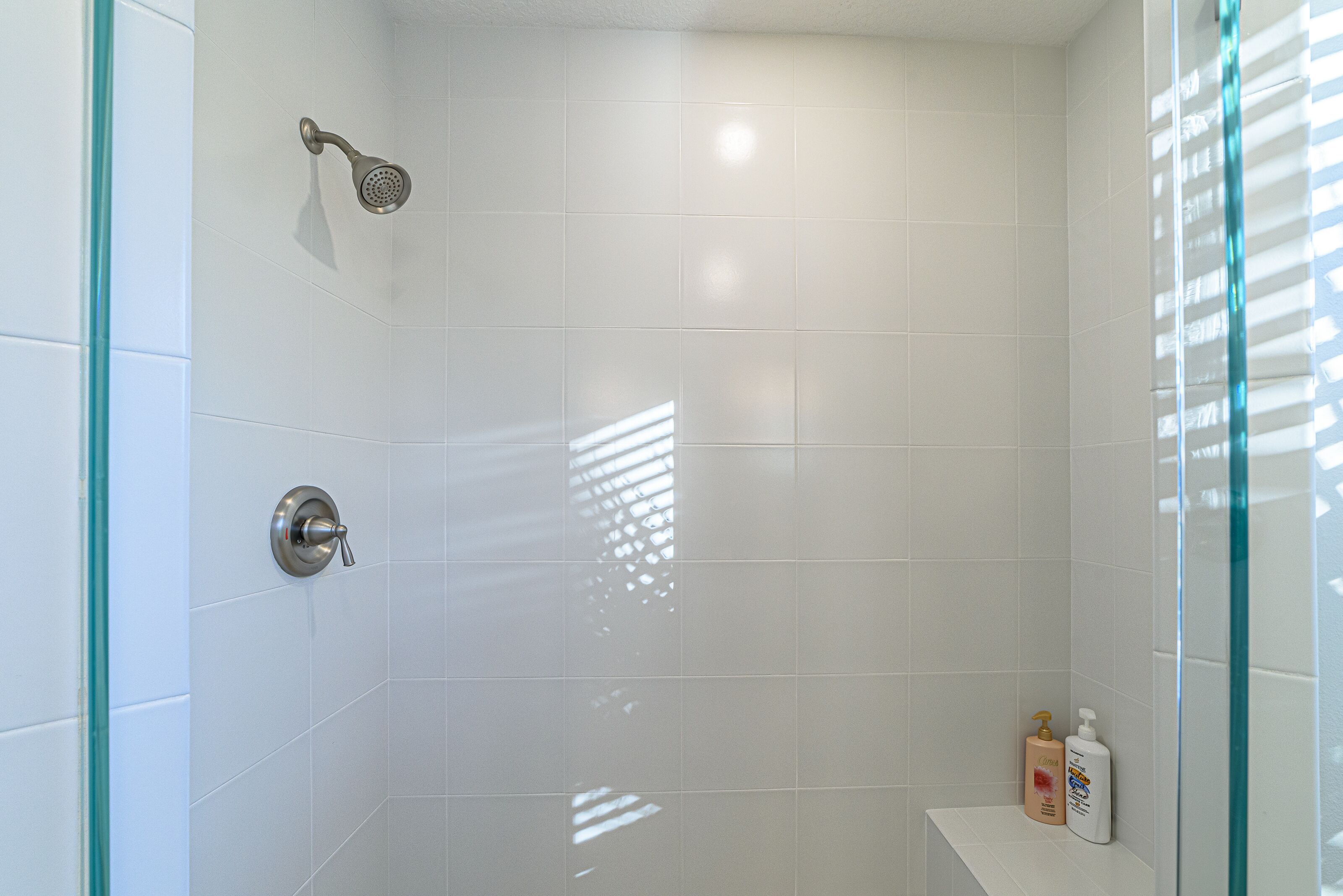A shower with white tiles, a glass door, and a shelf with toiletries.