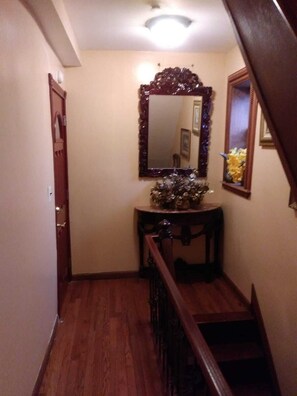 A wooden staircase with a handrail, a mirror with a decorative frame, and a small table with a vase of flowers. - East 42nd Mansion (Brooklyn)