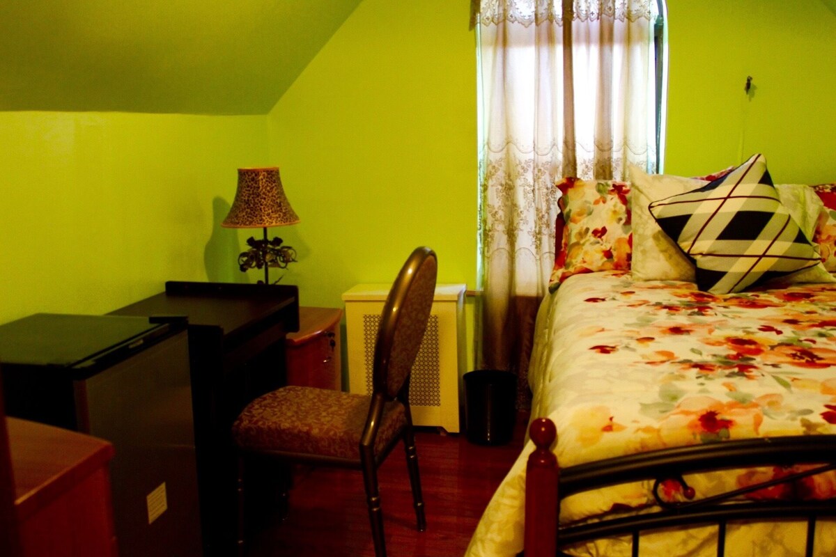 A bedroom with a bed, a desk, a chair, a lamp, and a window with curtains.