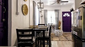 A dining area with a table set for four, chairs with patterned cushions, a ceiling fan, and a purple door in the background. - Purple Cottage, Hidden Gem near Hummingbird Beach (Soufriere)