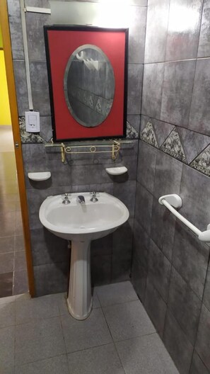 Une salle de bain avec un lavabo sur colonne, un miroir et une barre d’appui.