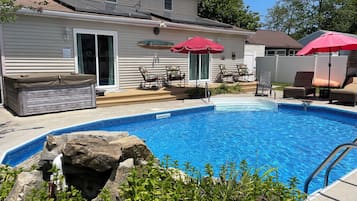 A backyard with a swimming pool, lounge chairs, and a hot tub.