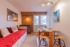 A cozy room with a bed, a dining table with chairs, and a view of the outdoors through a door.