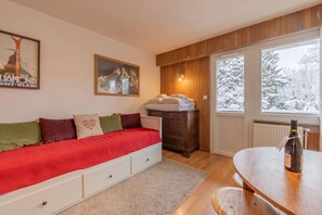 Une pièce confortable avec un lit, une commode, une fenêtre donnant sur des arbres couverts de neige et une bouteille de vin posée sur une table.