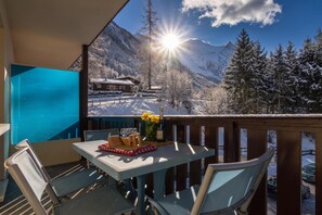 A balcony with a table set for two, overlooking a snowy mountain landscape.