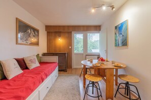 A cozy room with a bed, a dining table with stools, and a view through a door.