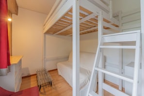 Une chambre avec un lit superposé, un plafond en bois, une petite table et un rideau rouge.