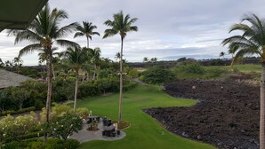 Um campo de golfe com um green bem cuidado, rodeado por palmeiras e formações rochosas vulcânicas.