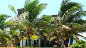 Um resort com várias palmeiras, piscina e um edifício com telhado de palha.