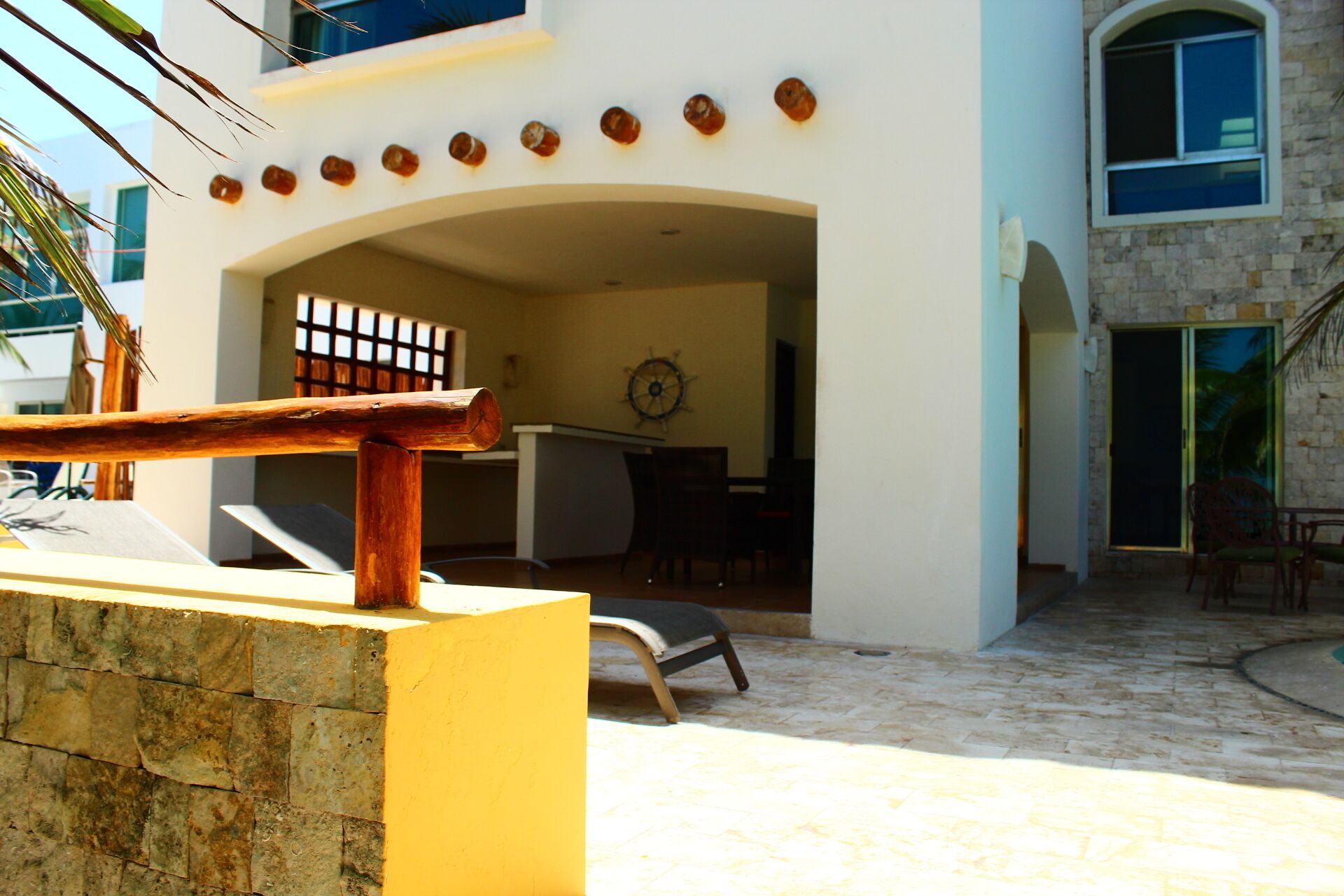 A modern building with a stone facade, a wooden bench, and a dining area with a sail wheel decoration.